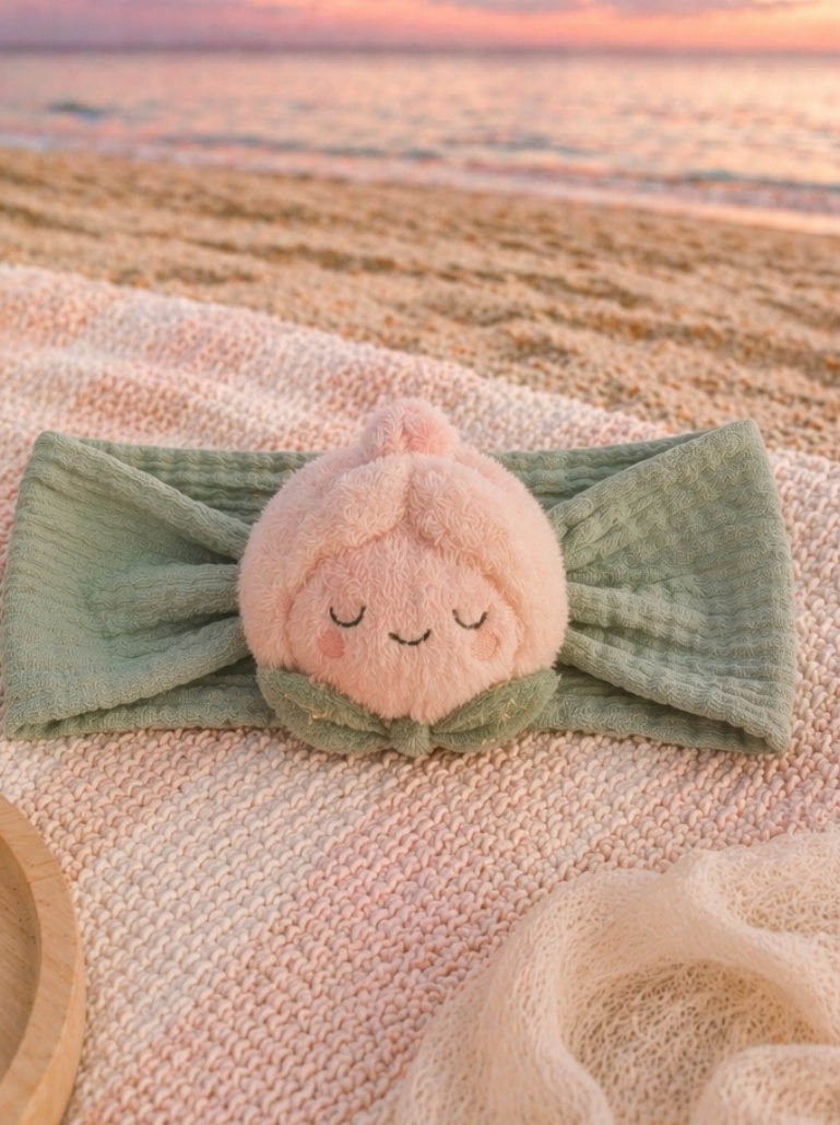 Baby-Headwrap mit schlafender Pfirsich-Plüschfigur – sanfte Bildsprache und B2B-Geschenkpotenzial